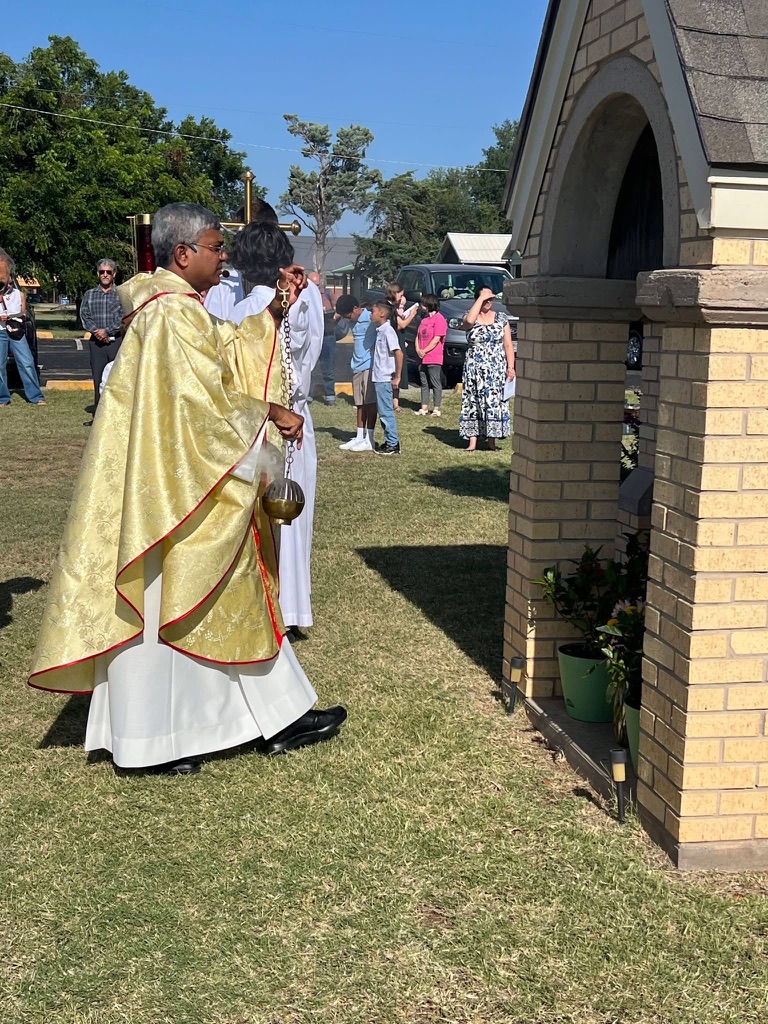 Fr. D swings a thurible to incense an outdoor shrine beside St. Ann Church while altar servers and parishioners observe.