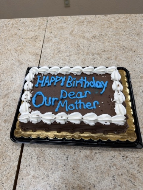 chocolate sheet cake decorated with white and blue frosting that read's "Happy Birthday Our Dear Mother."