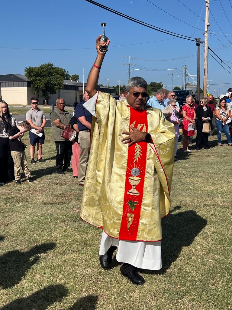 Fr. D raises an aspergillum to sprinkle holy water over parishioners gathered outside St. Ann Church.