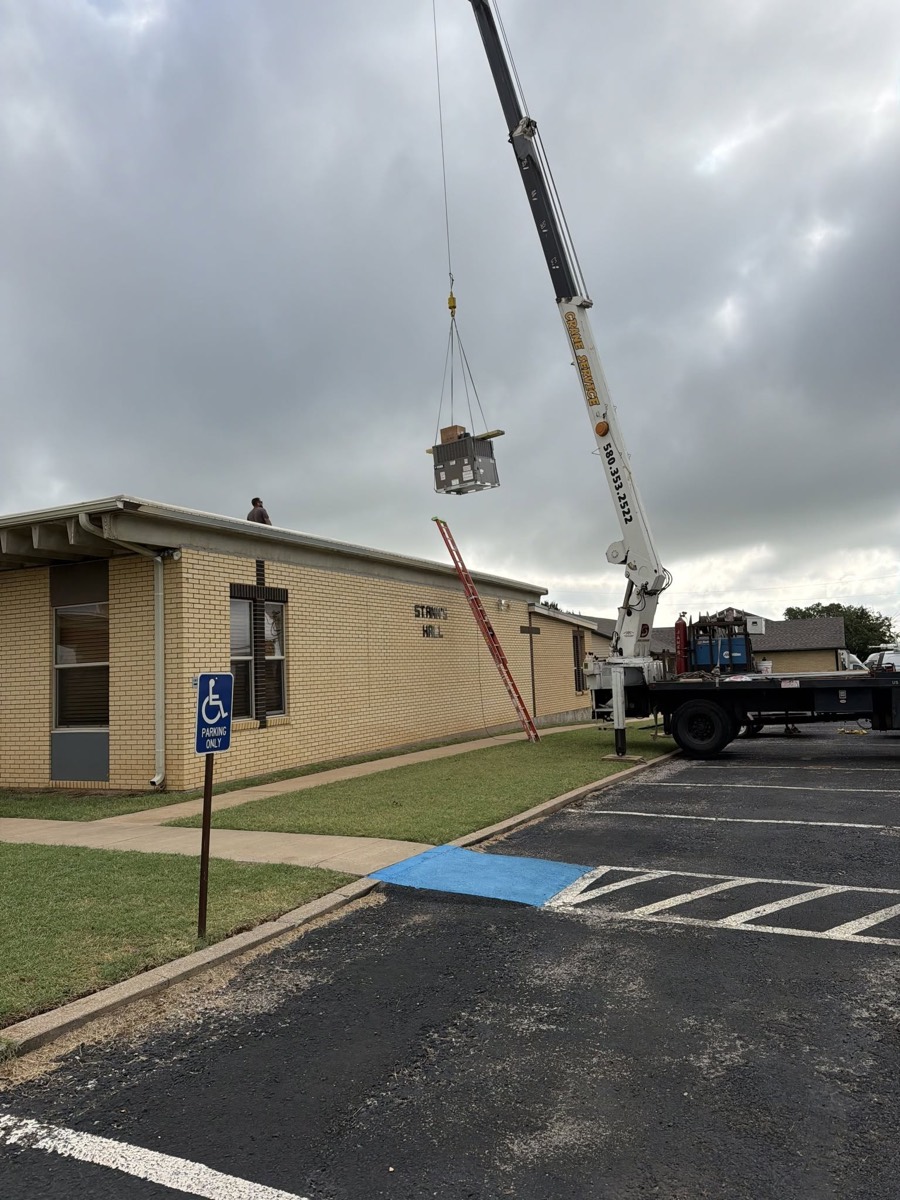A crane lifting new air-conditioning equipment onto the roof of St. Ann Parish Hall