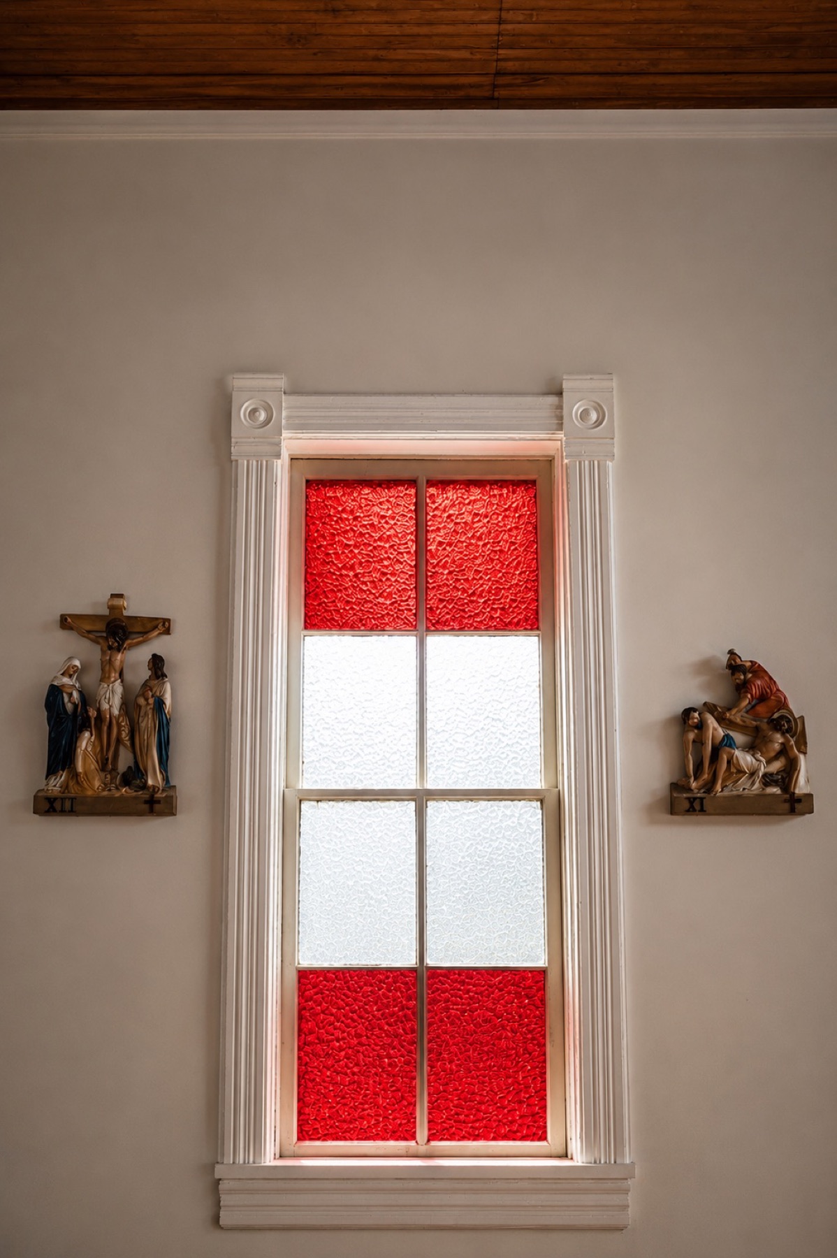 Red and white church window between Stations of the Cross at Mother of Sorrows